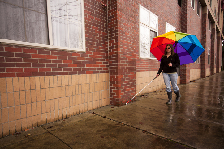 young blink woman walks with an umbrella and walking stick in the rain