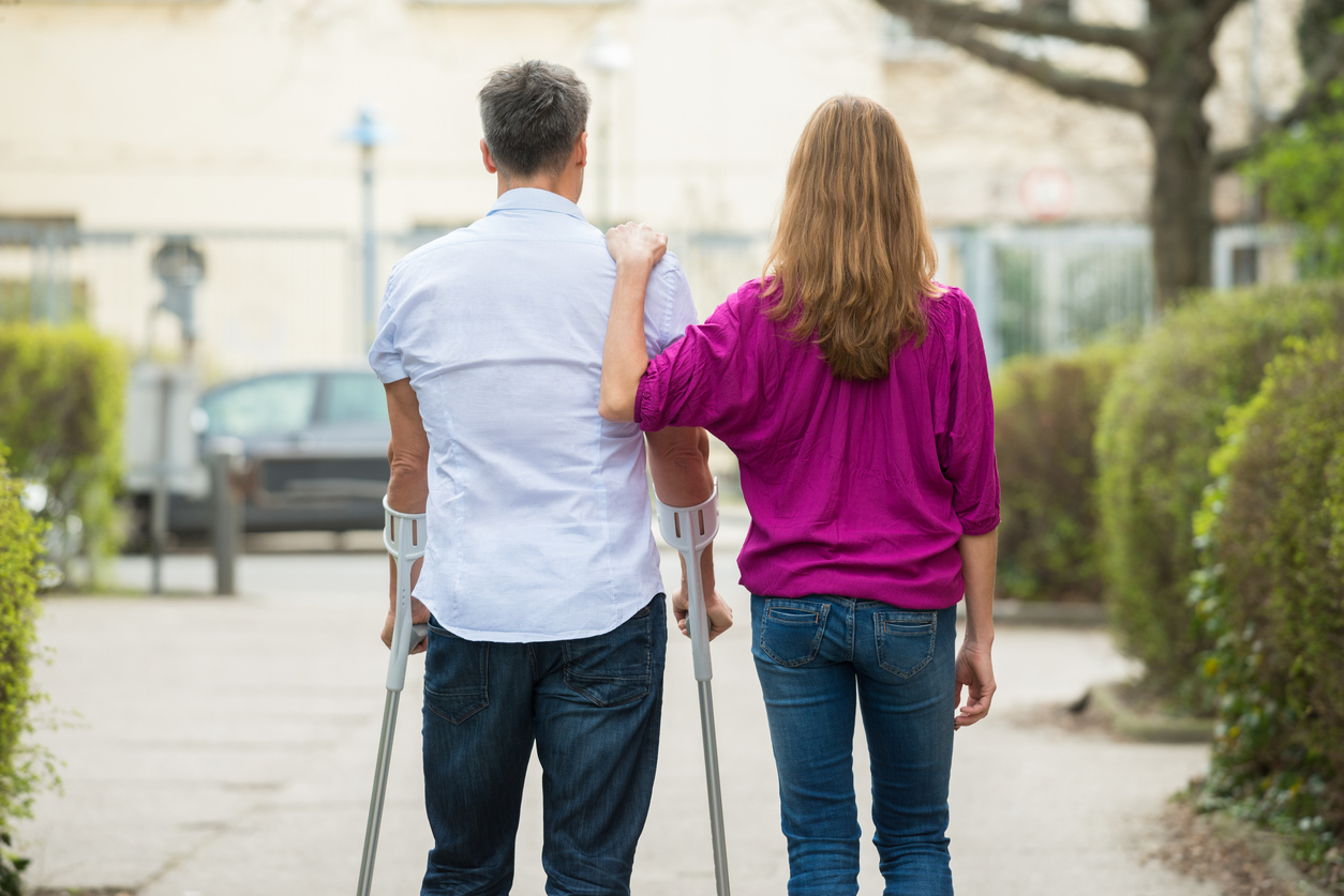 young woman with hand on shoulder of a man using crutches