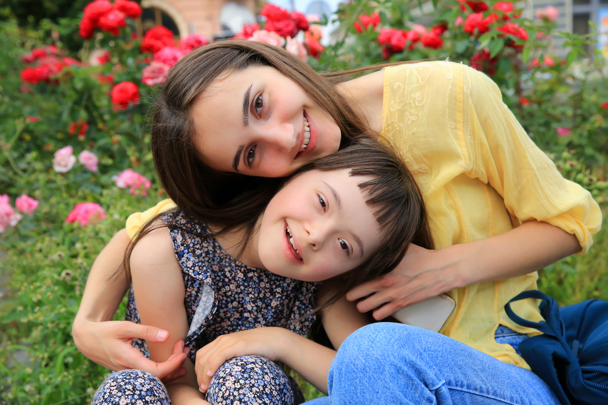 young woman and down syndrome child smile in a garden